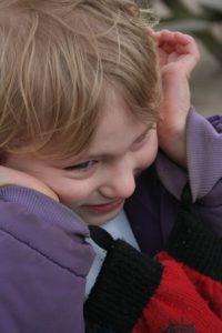 An autistic child trying to shut out noise by covering his ears.