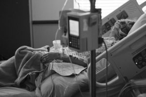 A patient lying in a hospital bed, hooked up to IV fluid.