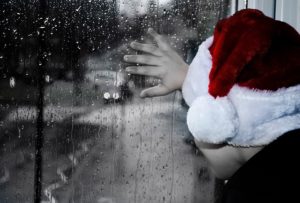 A child wearing a Santa Hat staring out the window waiting in anticipation.