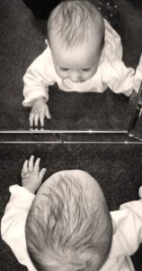 A baby exploring their reflection in a mirror.