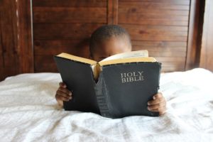 A child reading the Holy Bible in bed.