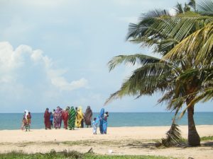 Women wrapped in colorful fabrics, walking on the beach in the distance.
