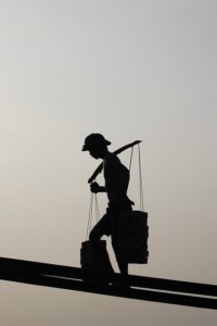 The silhouette of a worker hauling a heavy load on their shoulders up platforms.