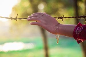 A hand reaching out to touch barbed wire.