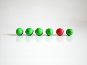 A row of green M&M's with one red one in the midst.