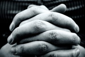 A black & white photo close-up of hands clasped together in prayer.