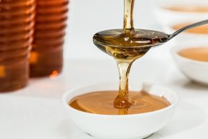 Honey being slowly poured into a spoon, overflowing into a saucer.