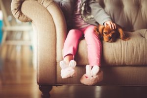 A child sitting on a sofa while petting a very relaxed puppy.