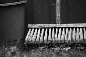 A black and white photo of a bucket and broom laid against the fence in a hard. 