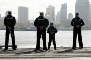A child dressed in a sailor's uniform standing next to Navy seamen.