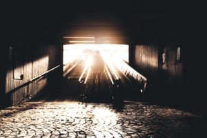 A sepia image of a person walking out of a tunnel into light.