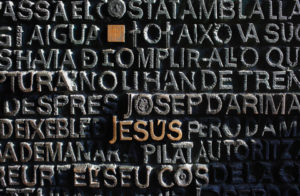 The word 'Jesus' standing out among words carved into a wall.