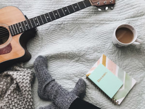 A person taking time to relax by enjoying a cup of coffee, journaling, and playing music.