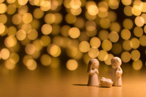 Figures of baby Jesus, Mary, and Joseph set before a background of twinkling lights.