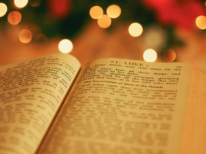 The Bible opened to the Christmas story in Luke in front of festive decorations.