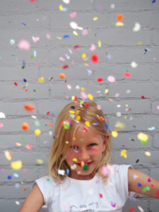 A child in the middle of colorful confetti tossed into the air.