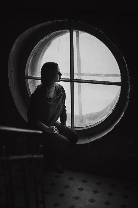 A person near a circle shaped window with a cross in it, surrounded in light.