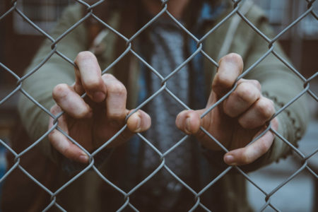Fingers gripping a chain link fence.