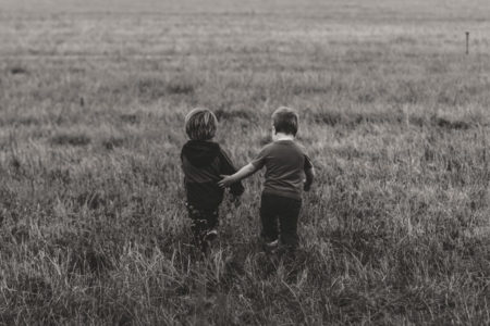 A child helping another as they walk in a field.