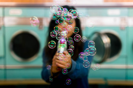 A woman blowing bubbles in a laundromat.