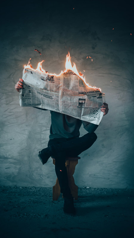 A man reading a newspaper that is engulfed in flames!