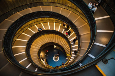 The view from the top of a winding stairwell with people walking down it.