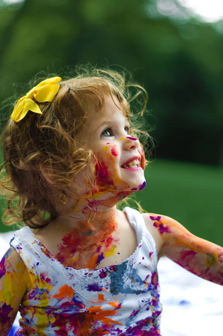 A little girl, smiling, covered in paint.