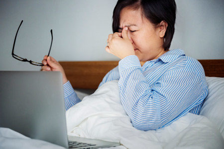 A person struggling to work on a laptop, while in bed.