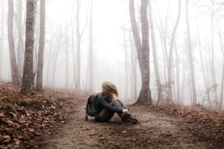A woman sitting on the ground in the middle of a foggy forest.