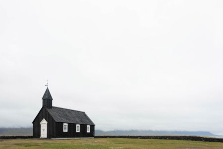 A church with green hills and overcast skies in the background.