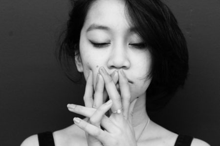 A woman with her fingers folded in front of her face, thoughtful.
