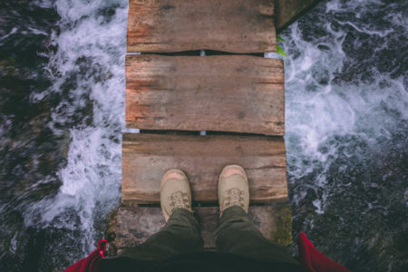 The view of someone's feet on a wooden bridge over water.