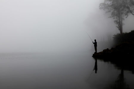 A man fishing in the fog.